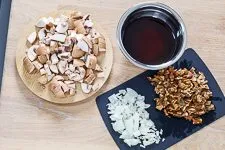 Geschnittene Champignons, Zwiebeln und eingeweichte Steinpilze auf einem Schneidebrett