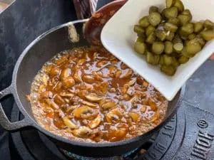 Geschnittene Essiggurken werden der Stroganoff-Sauce hinzugefügt