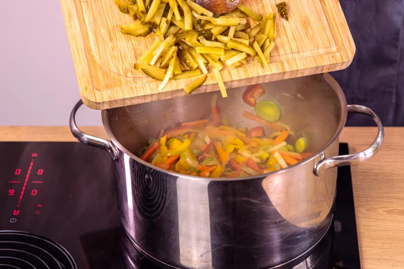 Geschnittene Gewürzgurken werden zum angebratenen Gemüse in den Topf gegeben