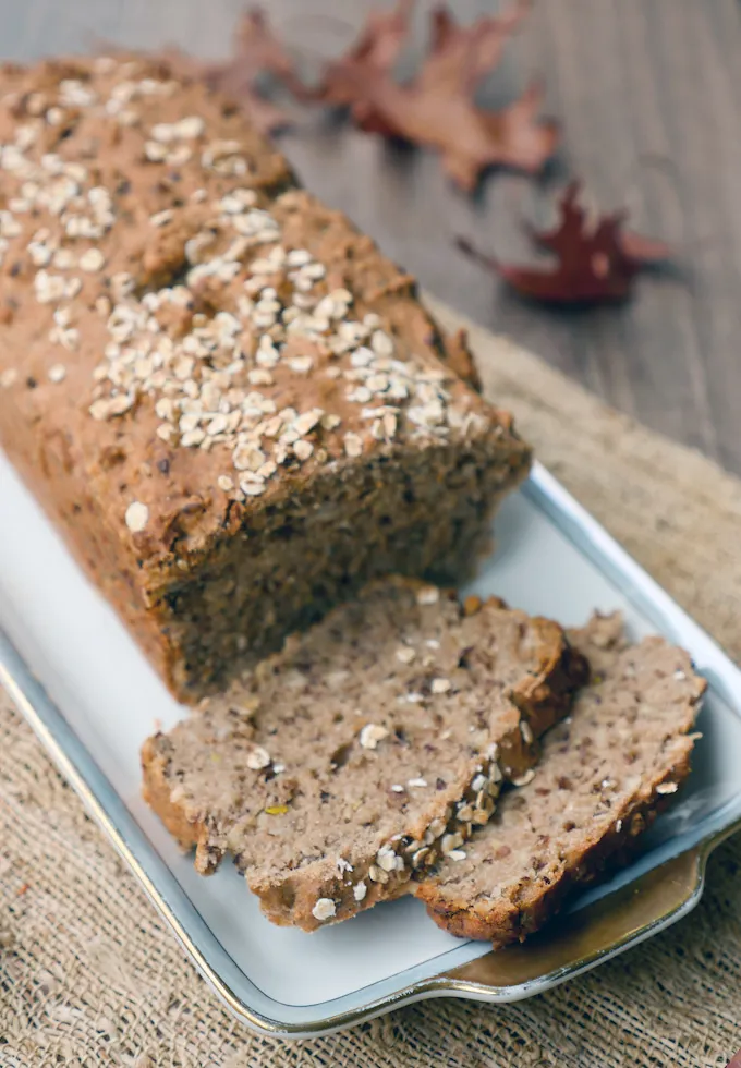 Geschnittenes Dinkel-Vollkornbrot mit Haferflocken bestreut, daneben ein Buch und ein Glas.