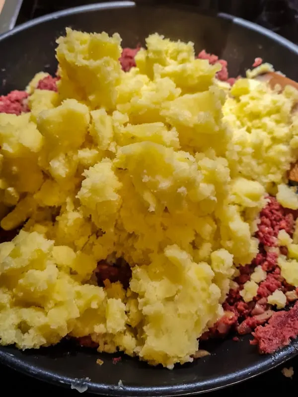 Gestampfte Kartoffeln zur Corned Beef-Zwiebel-Mischung in die Pfanne geben