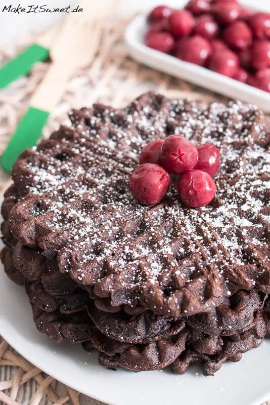 Gestapelte Schokowaffeln mit Puderzucker und frischen Kirschen, perfekt für ein deutsches Frühstück oder Dessert