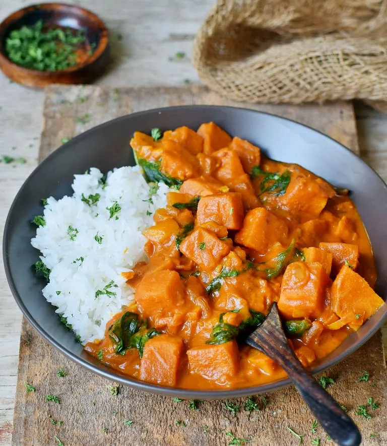 gesundes veganes Süßkartoffel-Curry, serviert mit Reis und frischem Spinat