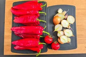 Gewaschene rote Spitzpaprika und Peperoni sowie halbierte Zwiebeln und Knoblauchzehen für Ajvar vorbereitet