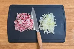 Gewürfelten Speck und geschnittene Zwiebeln auf einem Holzbrett, bereit für das Anbraten beim Sauerkraut kochen