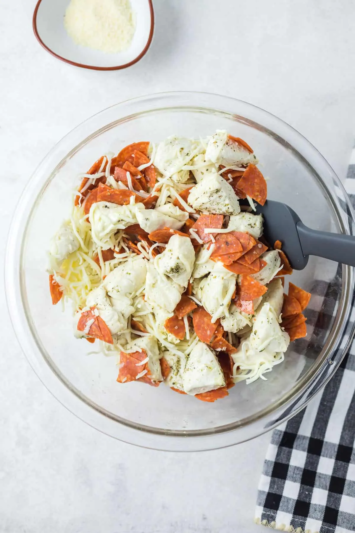 Gewürzte Keksteigstücke, geriebener Käse und gewürfelte Peperoni in einer Glasschüssel vermischt.