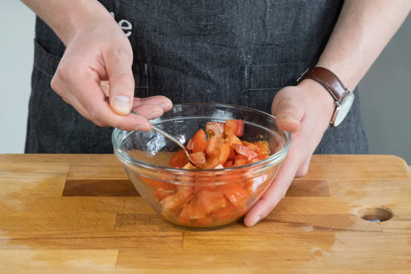 Gewürzte Tomatenwürfel werden für die Tajine vermischt