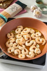 Goldbraun angebratene Garnelen in einer Pfanne mit Knoblauch.