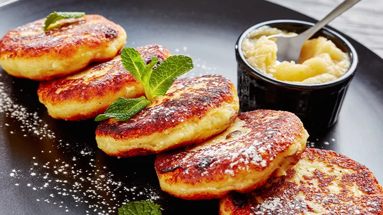 Goldbraun gebratene Quarkkeulchen, serviert mit einer Schale frischem Apfelmus, ein süßer Klassiker.