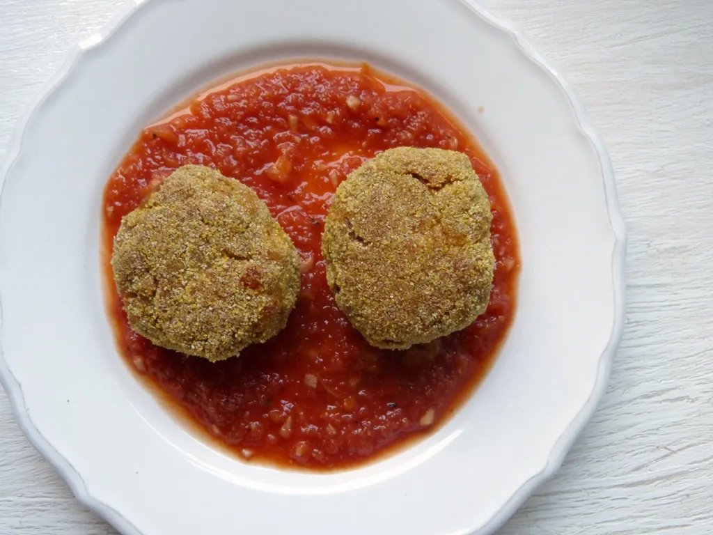 Goldbraune Buchweizenfrikadellen auf einem Bett aus reichhaltiger Tomatensauce, garniert mit frischen Kräutern.