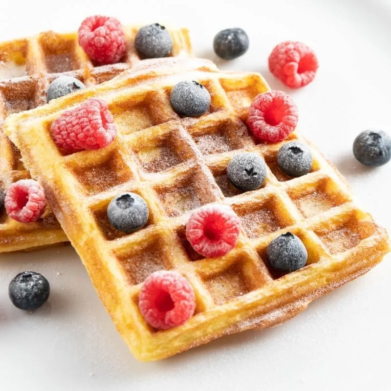 Goldbraune Keto Waffeln, garniert mit Beeren und Puderzuckerersatz, ideal für ein süßes Low Carb Frühstück.