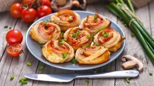 Goldbraune Schinken-Käse-Blätterteigschnecken auf einem Backblech.