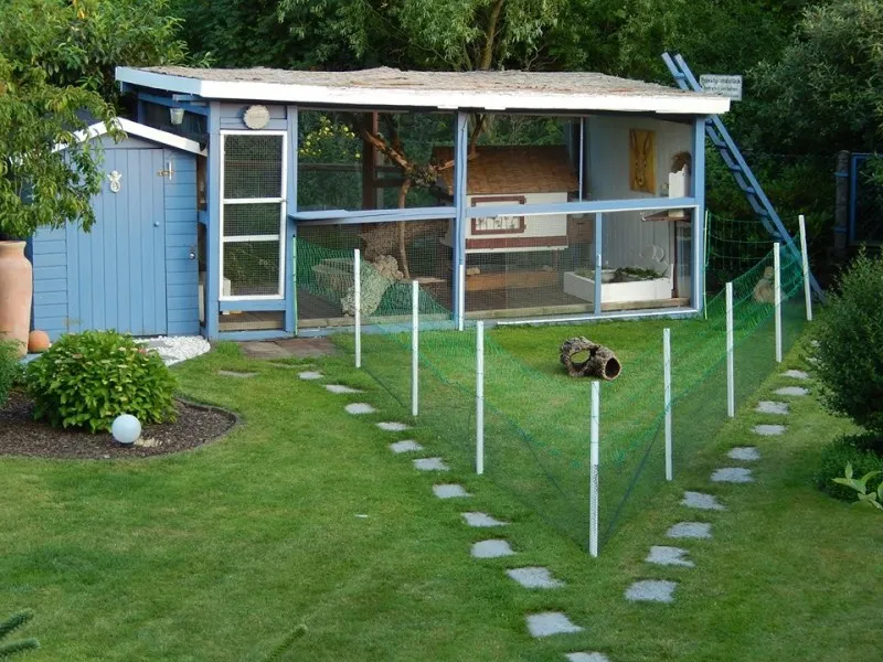 Große Kaninchenvoliere als sicherer Außenauslauf mit vielfältigen Strukturen für Hasen als Haustier im Garten