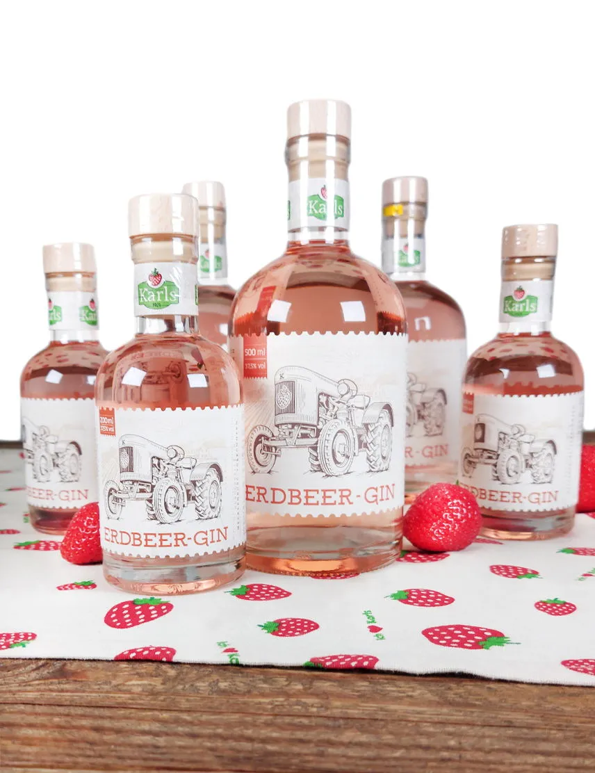 Große und kleine Flasche Karls Erdbeer-Gin umgeben von reifen Erdbeeren