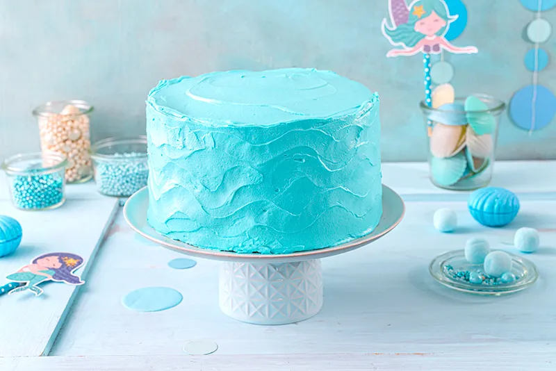 Grundierte Meerjungfrauen-Torte mit kunstvollen Wellenstrukturen am Rand, bereit für die finale Dekoration