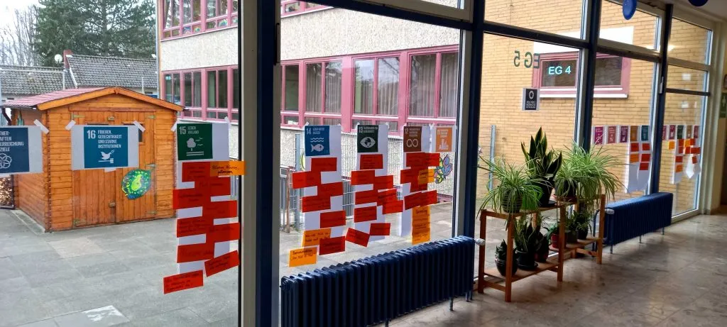 Grundschulkinder betrachten Plakate mit Ideen für die Projektwoche Nachhaltigkeit in der Pausenhalle.