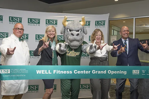 Gruppenfoto der USF Health Führungskräfte und Rocky dem Bullen vor dem Banddurchschnitt zur Eröffnung des Fitness Centers