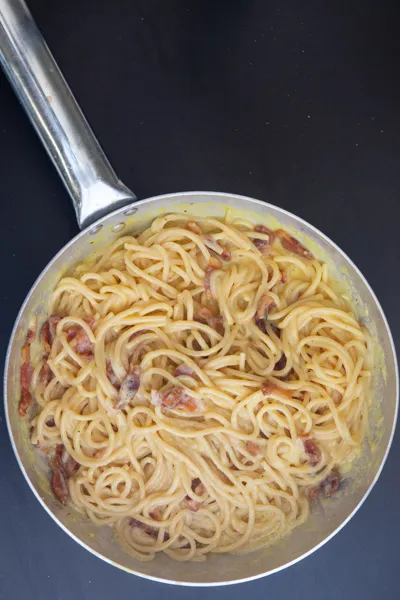 Guanciale wird zu den Spaghetti in die Pfanne gegeben, ein entscheidender Schritt für die authentische Carbonara