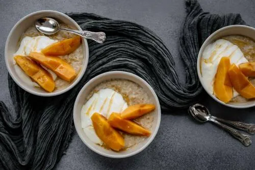 Haferporridge mit Joghurt und Quittenkompott in drei Schüsseln vor dunklem Hintergrund.
