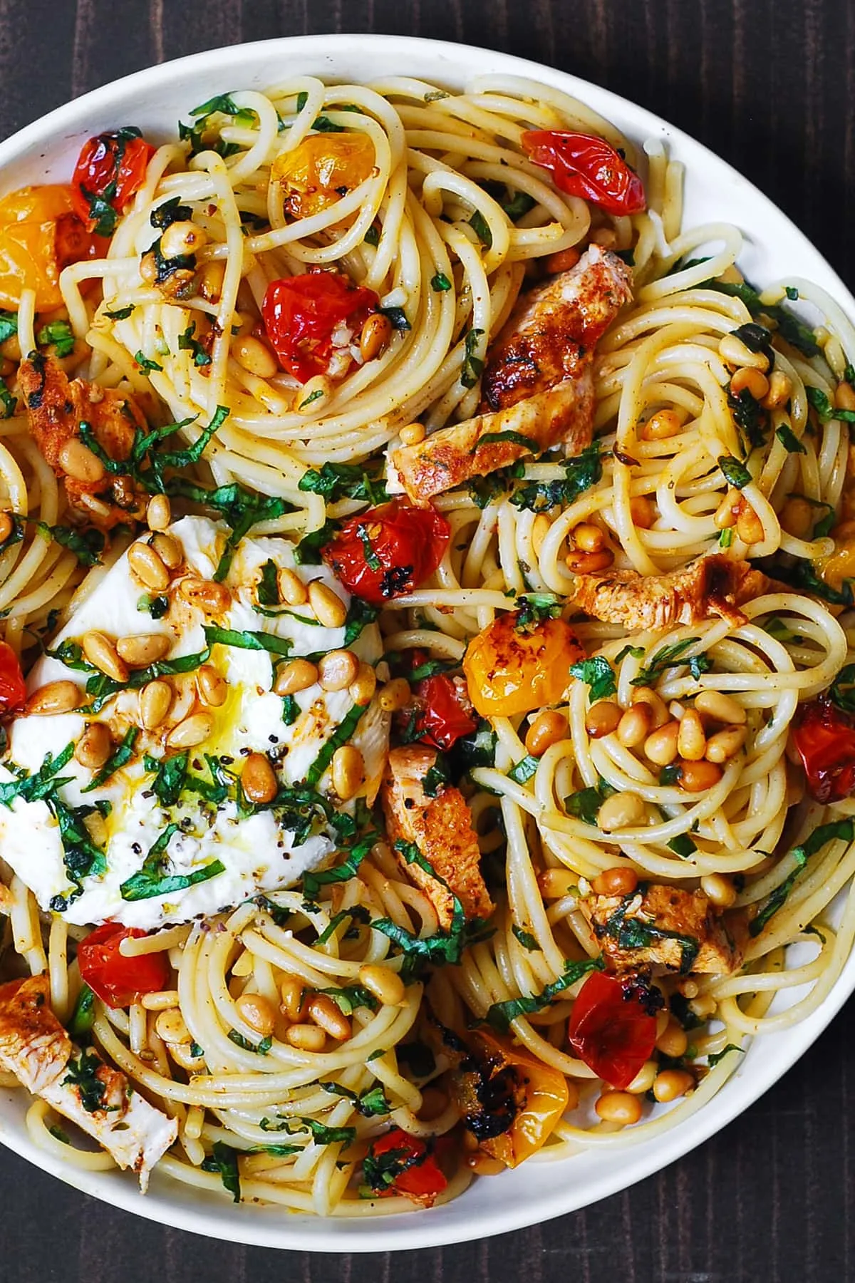 Hähnchen Spaghetti mit cremiger Burrata, gerösteten Kirschtomaten und goldbraunen Pinienkernen auf einem weißen Teller serviert.