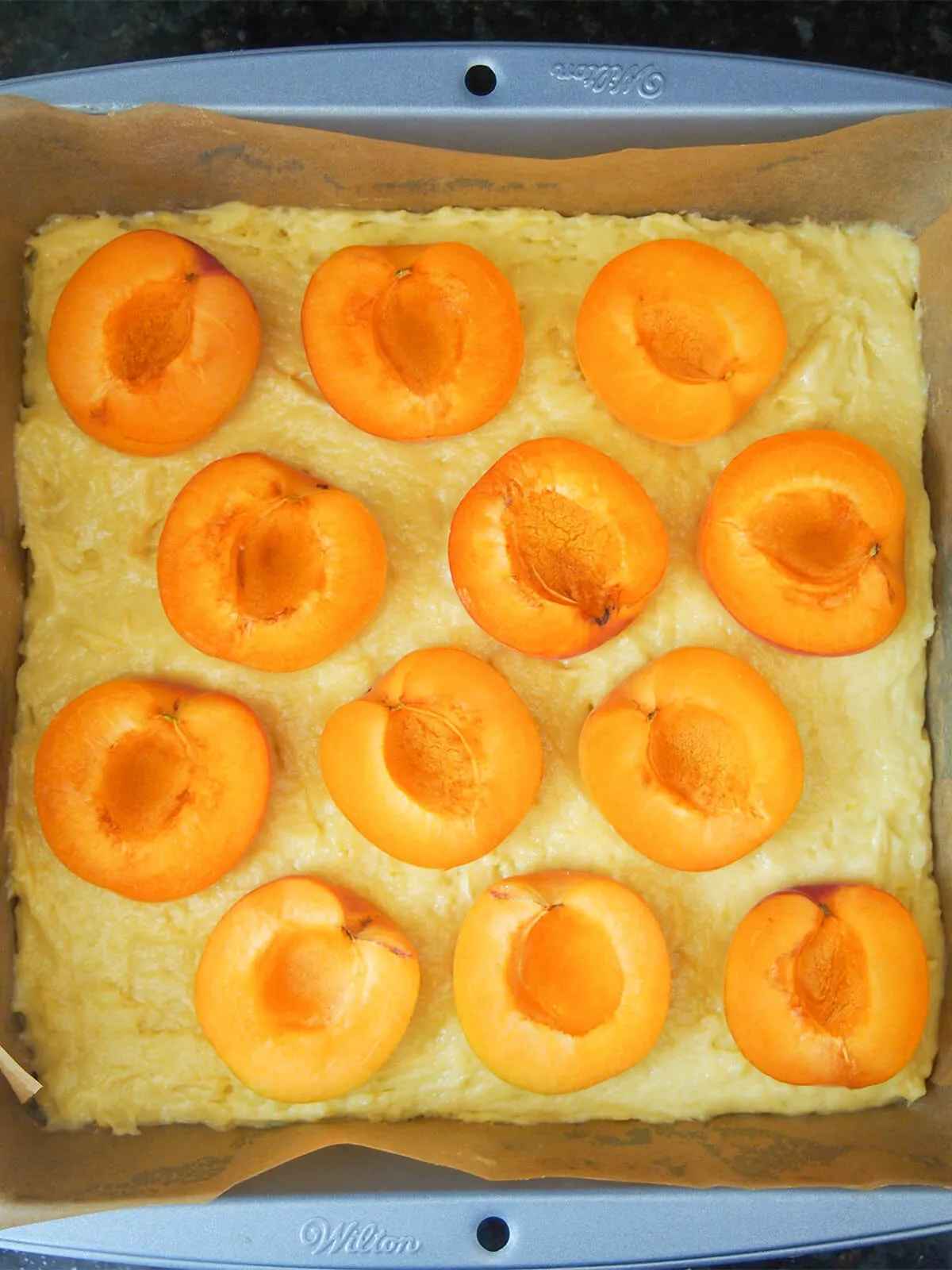 Halbierte Aprikosen liegen auf dem Kuchenteig in einer Backform, bereit zum Backen