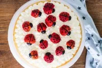 Halbierte Erdbeeren und Heidelbeeren, die als Marienkäfer auf dem Kuchen arrangiert sind