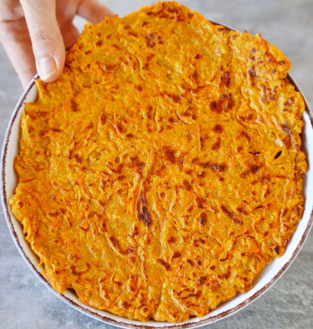 Hand hält Teller mit Karotten-Fladenbrot