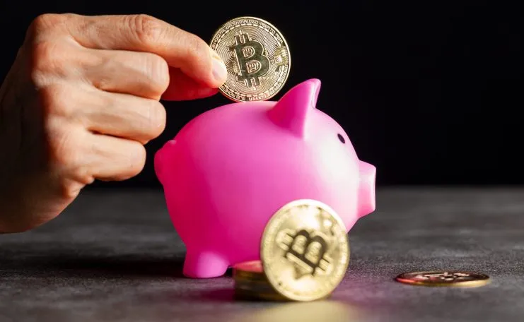 Hand legt Bitcoin in Sparschwein, symbolisiert Amazons Potenzial zur Förderung digitaler Zahlungen und Krypto-Adoption.