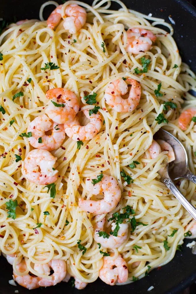 Hand rührt Scampi und Spaghetti mit einer Zange in einer Pfanne, vermischt mit Weißwein-Knoblauch-Sauce.