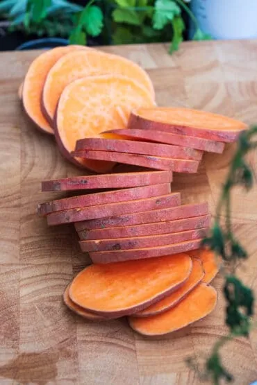 Hand schneidet eine Süßkartoffel präzise in fingerdicke Scheiben, essenziell für ein gleichmäßiges Süßkartoffel grillen.