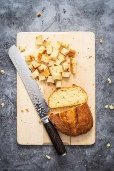 Hand schneidet frisches Ciabatta in mundgerechte Würfel für den Panzanella Brotsalat