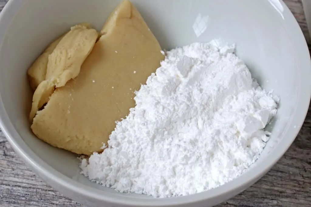 Hände kneten Marzipan mit Puderzucker in einer Schüssel, ein entscheidender Schritt bei der Zubereitung von Marzipankartoffeln