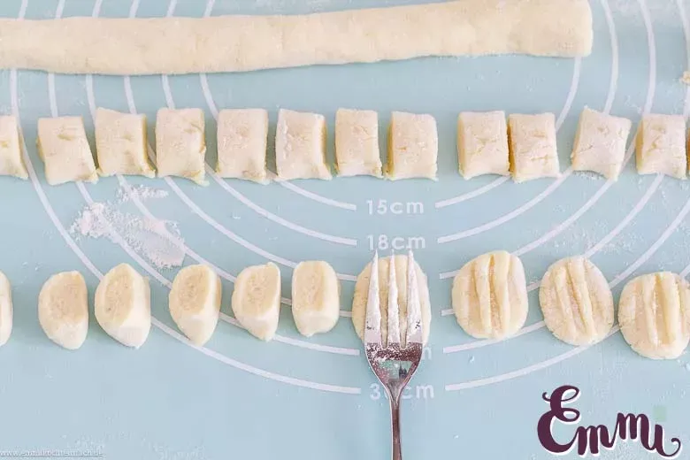 Hände rollen Gnocchi-Teig auf einer bemehlten Arbeitsfläche zu langen Strängen, als Teil eines einfachen Rezepts.