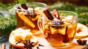 Hausgemachter Bratapfelglühwein in weihnachtlichen Tassen, mit Zimt und Apfelstücken garniert