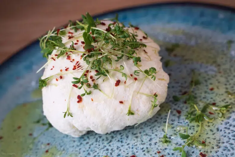 Hausgemachter Frischkäse mit frischer Kresse und Olivenöl auf einem rustikalen Teller serviert.