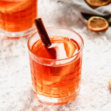 Heißer Aperol in Whiskeygläsern mit Orangen- und Zimtdekor auf verschneitem Hintergrund.