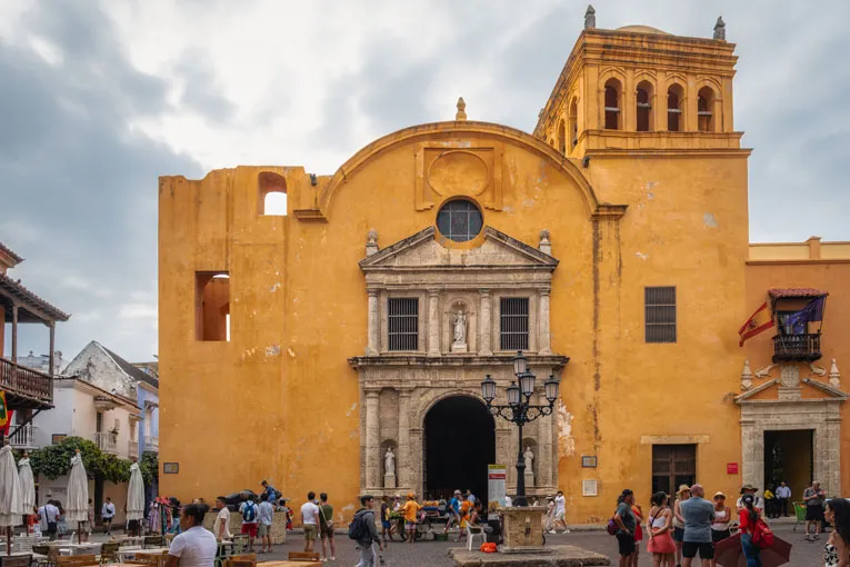 Historische Kirche mit gelber Fassade und imposantem steinernem Eingang, im Vordergrund Menschen
