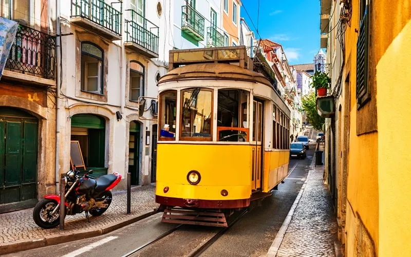 Historische Straßenbahn fährt durch eine enge Gasse in Lissabon, Portugal