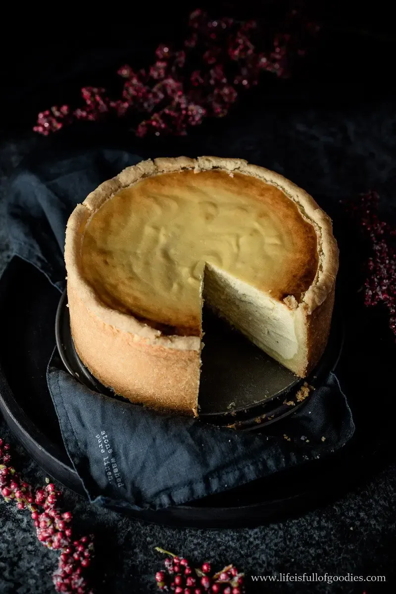 Hoher, cremiger Käsekuchen mit goldbraunem Rand auf weißem Teller
