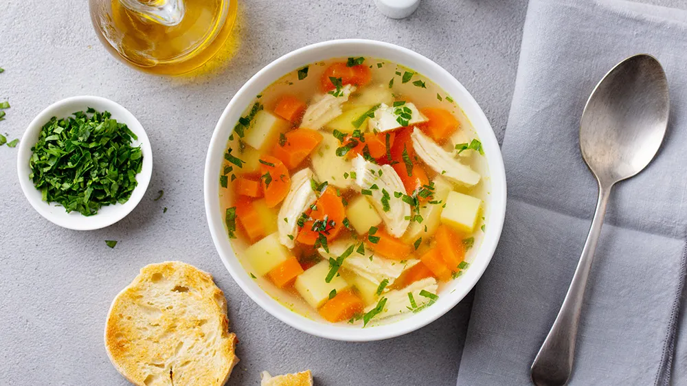 Hühnerbrühe mit frischer Einlage aus Huhn und Gemüse in einer tiefen Schale.