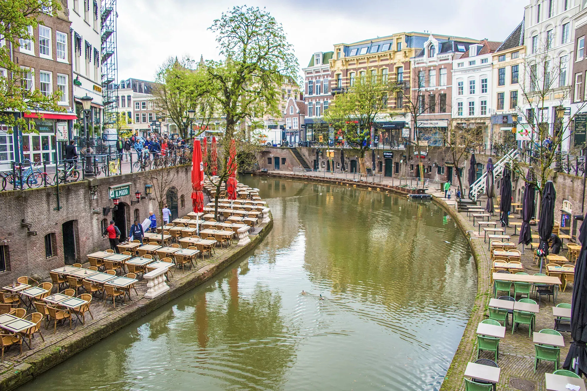 Idyllische Kanalszene in Utrecht mit Terrassen, roten Sonnenschirmen und klassischen Gebäuden am Wasser.