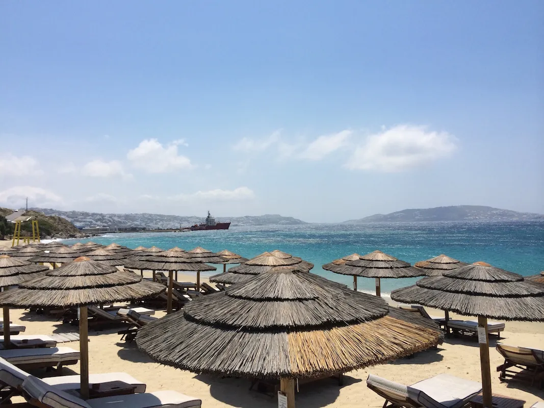 Idyllischer Strandabschnitt in Agios Stefanos, Mykonos, mit kleinen Booten und Blick auf die Stadt, ideal für entspannten Urlaub