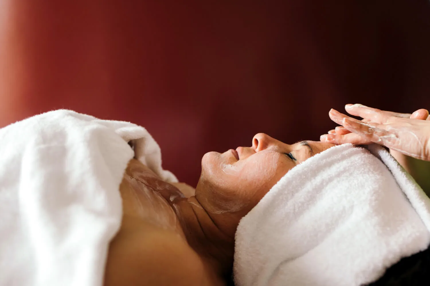 In Frottee gewickelte liegende Frau bekommt eine Gesichtsbehandlung