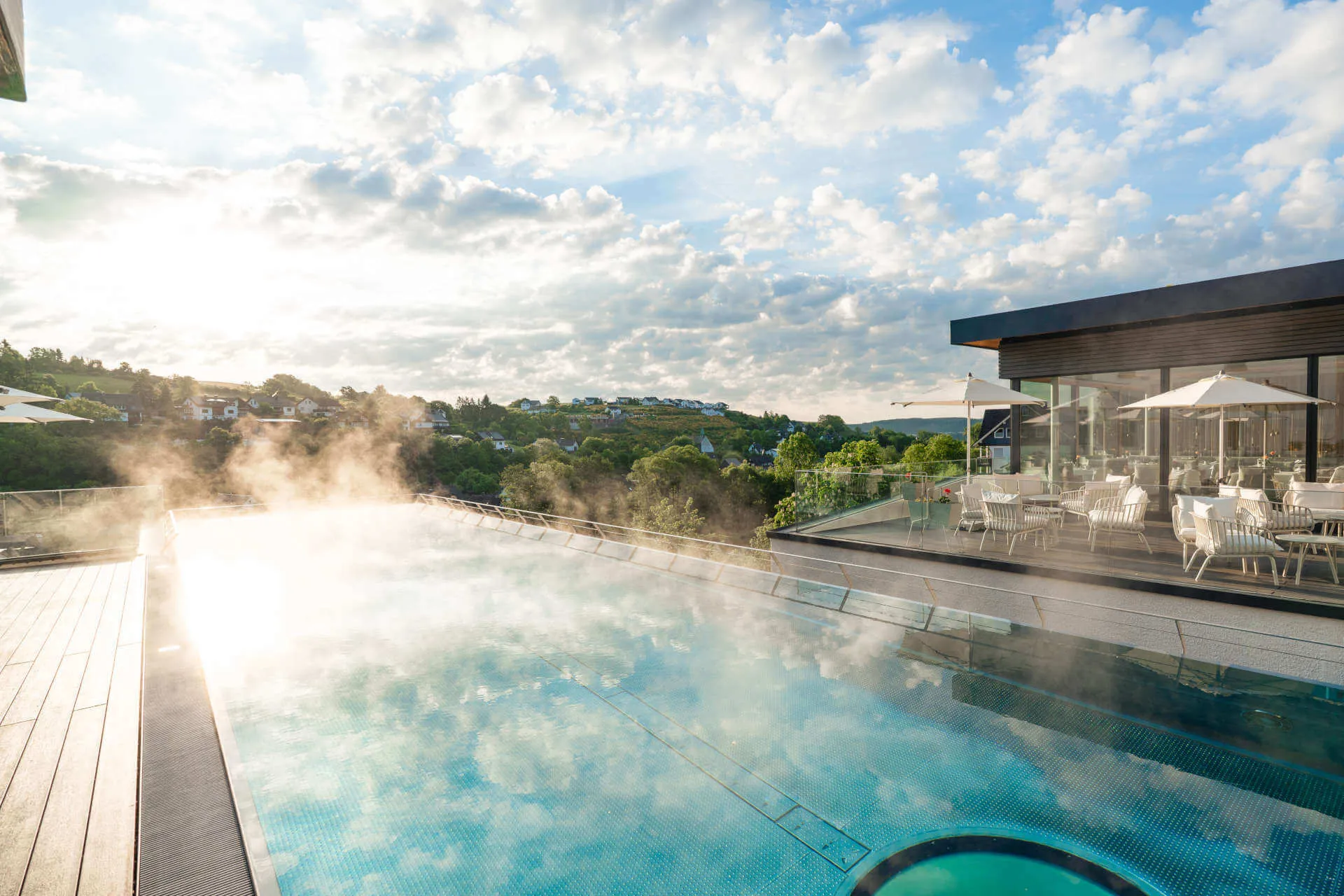 Infinitypool bei Sonnenaufgang mit aufsteigendem Dampf und Blick auf das Tal und die Terrasse.