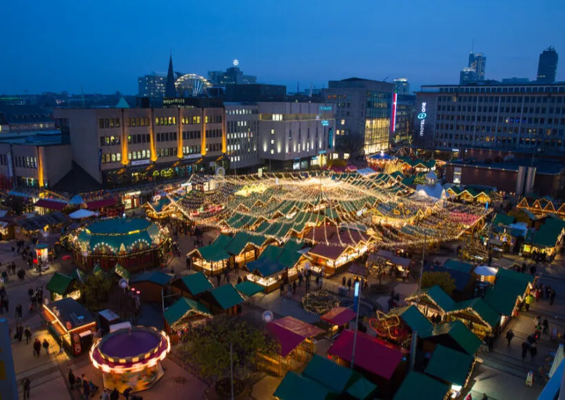 Internationaler Weihnachtsmarkt Essen bei Nacht, beleuchtet vom Lichterglanz, mit Besuchern und festlicher Stimmung.