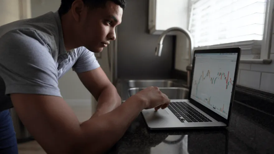 Junger Mann nutzt eine Neo-Broker App auf seinem Laptop für den Wertpapierhandel