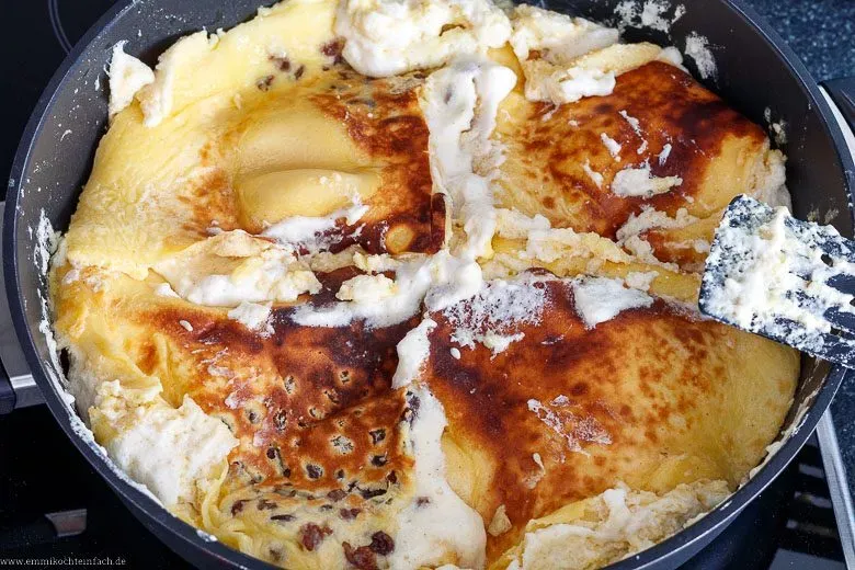 Kaiserschmarrn-Teig backt in einer großen Pfanne goldbraun aus, kurz bevor er gewendet und zerrissen wird. Wichtiger Schritt beim Kaiserschmarrn selber machen.