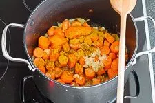 Karotten, Zwiebeln, Ingwer und Currypulver werden in einem Topf angedünstet, um die Aromen für die Karotten Ingwer Suppe zu entfalten.
