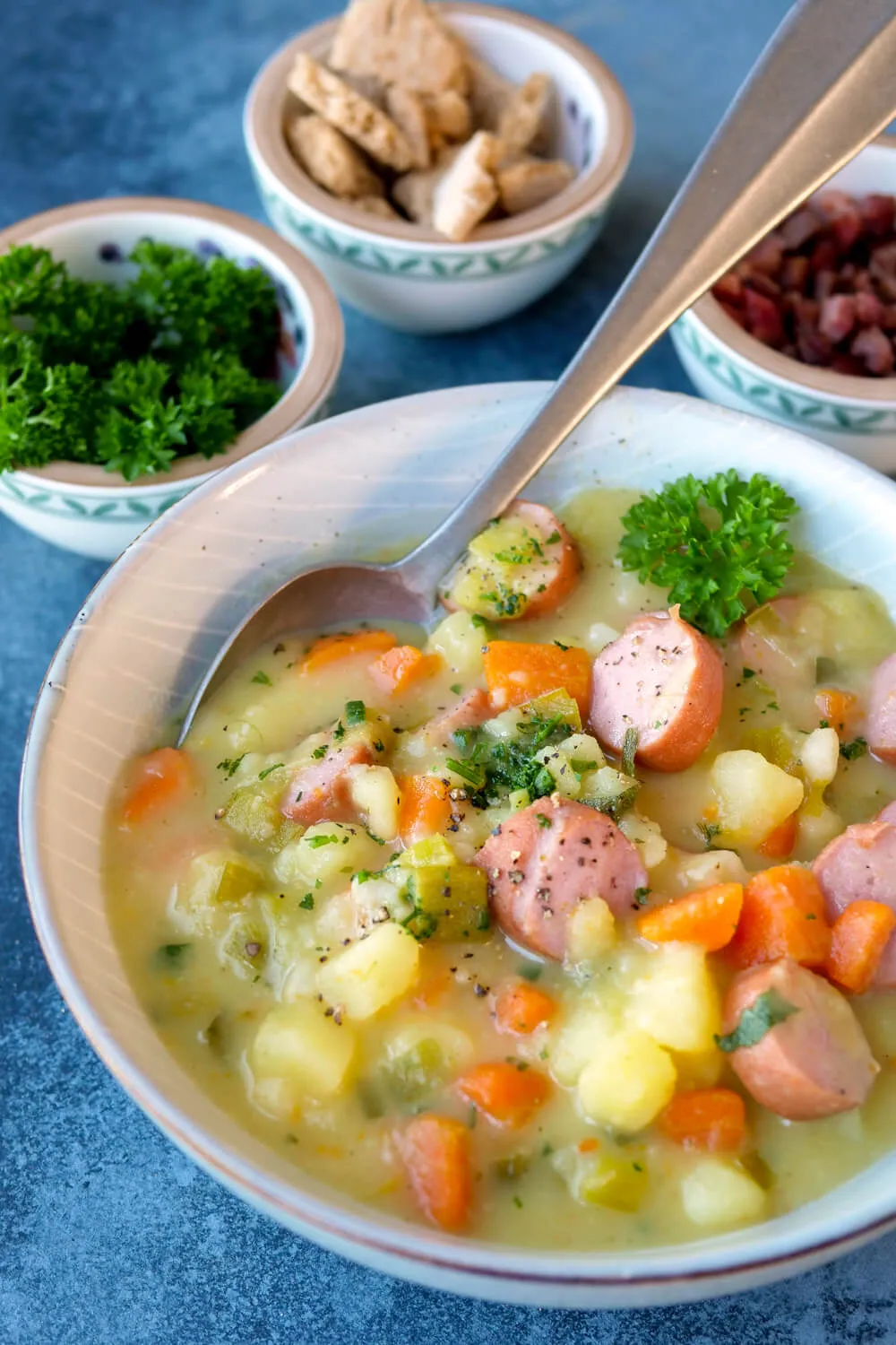 Kartoffelsuppe mit Würstchen, Suppengemüse und frischer Petersilie in einer tiefen Schüssel