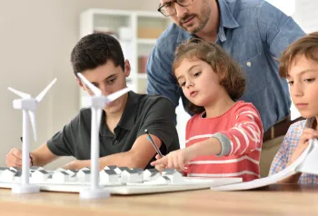 Kinder lernen im Klassenzimmer über erneuerbare Energien, mit einer Windkraftanlage im Hintergrund